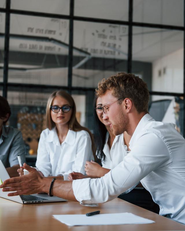 Drei Personen sitzen an einem Tisch in einem modernen Büro und schauen auf einen Laptop Drei Personen sitzen an einem Tisch in einem modernen Büro und schauen auf einen Laptop