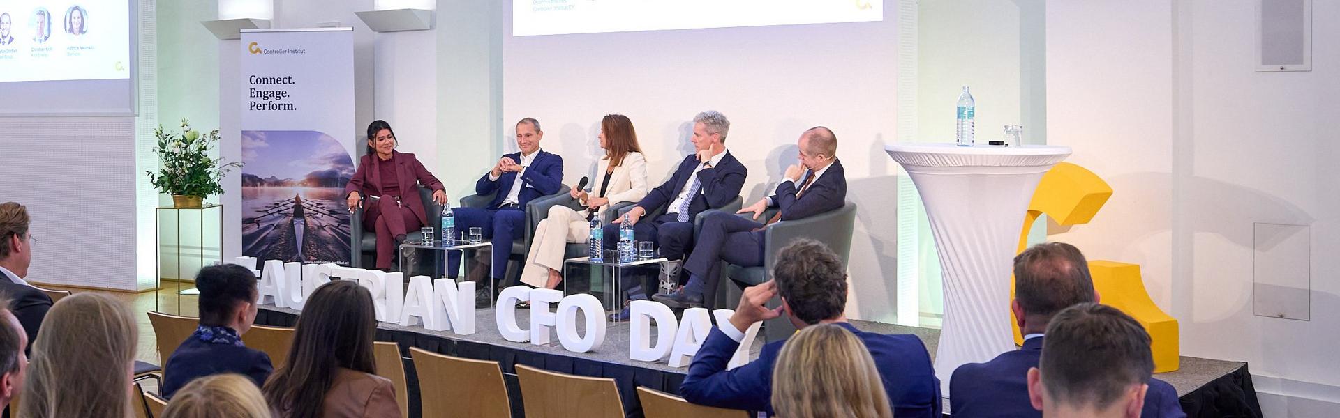Austrian CFO Day 2025 Podiumsdiskussion mit fünf Personen vor Publikum in einem Saal mit Kronleuchtern und Präsentationsbildschirmen