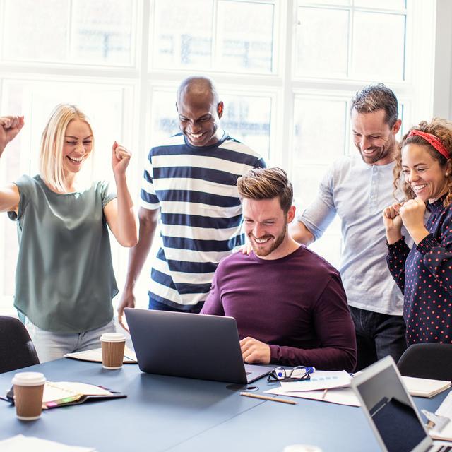 Fünf Personen in einem Büro feiern gemeinsam vor einem Laptop, sichtbar erfreut und motiviert