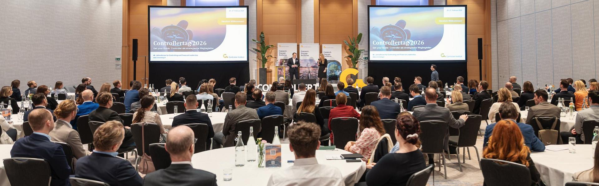 Controllertag_2026 Konferenzsaal mit Publikum, das auf zwei große Bildschirme und eine Bühne mit Rednern blickt