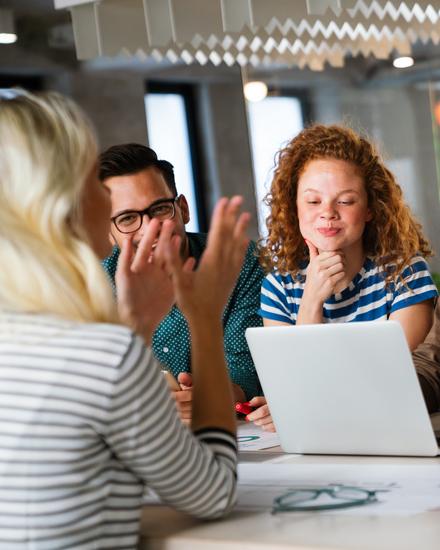 Ein Team von sechs jungen Personen sitzt an einem Tisch um einen Laptop und diskutiert