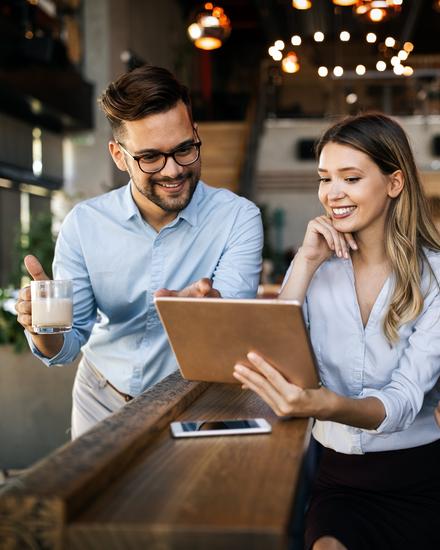 Drei junge Berufstätige in Büro mit Tablet, eine Frau zeigt zwei Männern etwas auf dem Bildschirm, alle lächeln