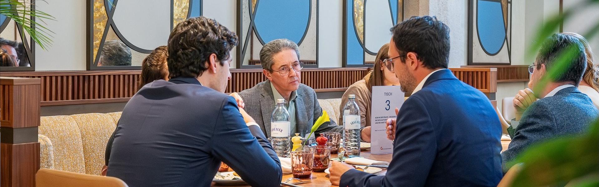Mehrere Personen sitzen an einem Tisch in einem modernen Restaurant mit großen Fenstern und dekorativen Elementen