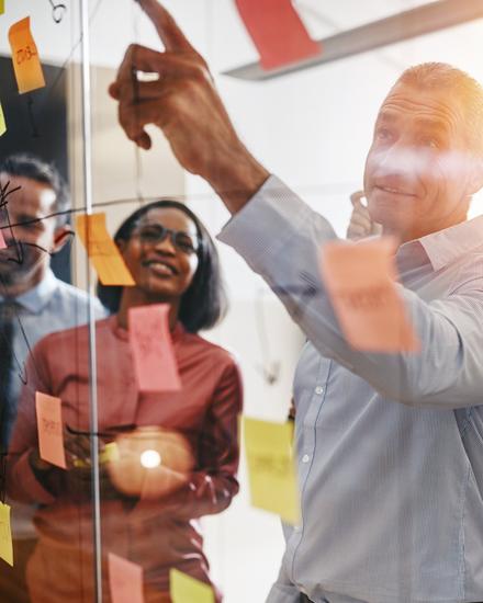 Team von fünf Personen diskutiert und plant mit bunten Haftnotizen an einer Glaswand in einem Büro