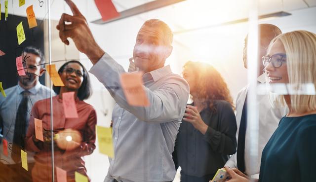 Team von fünf Personen diskutiert und plant mit bunten Haftnotizen an einer Glaswand in einem Büro