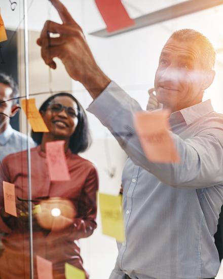 Team von fünf Personen diskutiert und plant mit bunten Haftnotizen an einer Glaswand in einem Büro