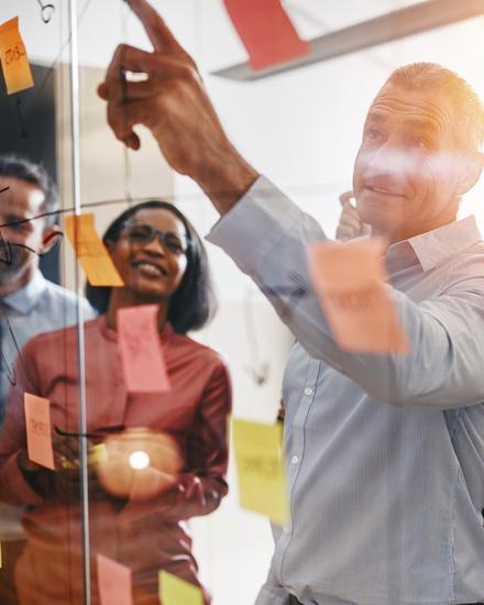 Team von fünf Personen diskutiert und plant mit bunten Haftnotizen an einer Glaswand in einem Büro
