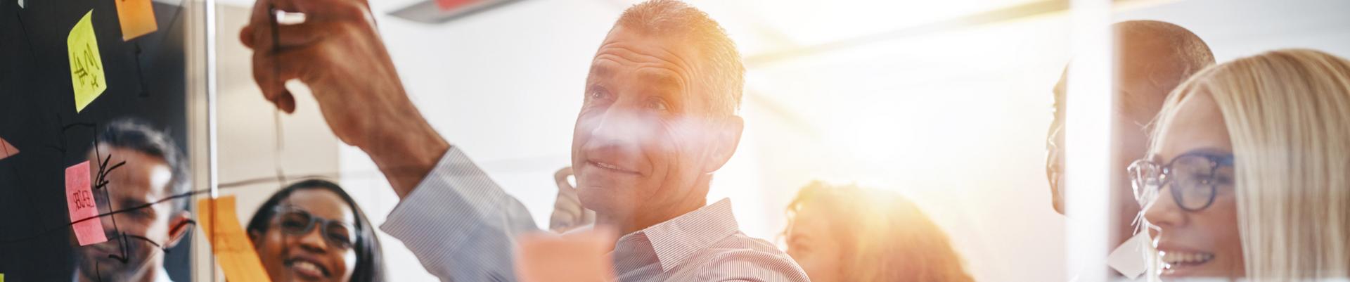 Team von fünf Personen diskutiert und plant mit bunten Haftnotizen an einer Glaswand in einem Büro