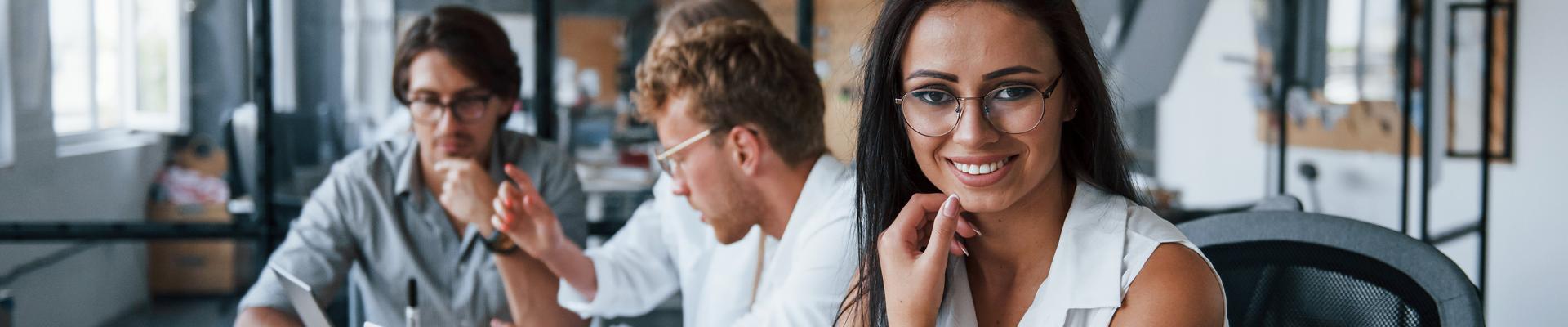 Drei Personen sitzen an einem Tisch mit Laptops und Unterlagen und arbeiten gemeinsam