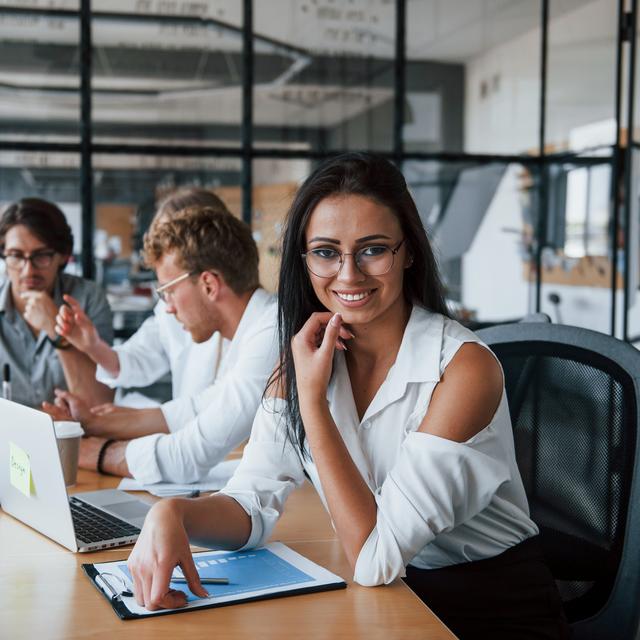 Drei Personen sitzen an einem Tisch mit Laptops und Unterlagen und arbeiten gemeinsam