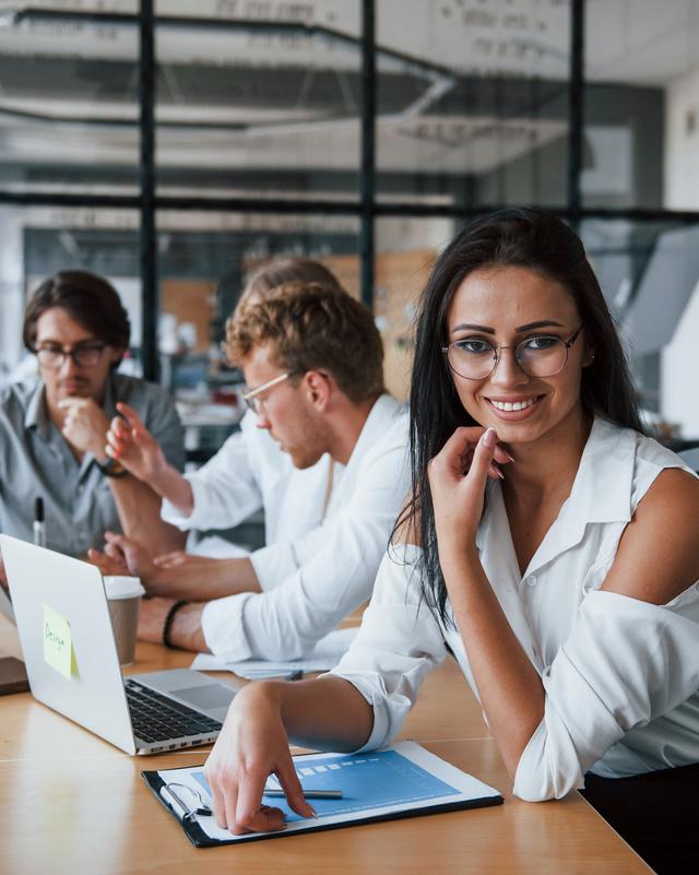 Drei Personen sitzen an einem Tisch mit Laptops und Unterlagen und arbeiten gemeinsam