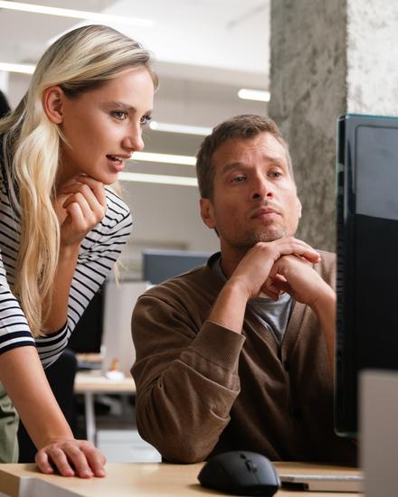 Zwei Kollegen arbeiten konzentriert gemeinsam an einem Computer in einem modernen Büro