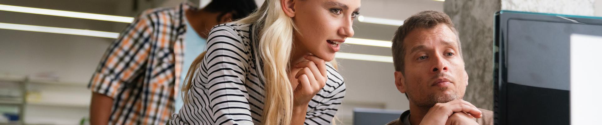 Zwei Kollegen arbeiten konzentriert gemeinsam an einem Computer in einem modernen Büro