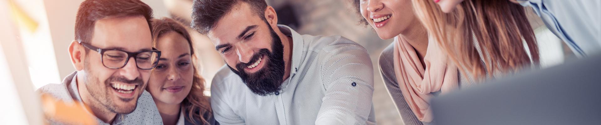 Fünf junge Erwachsene schauen lächelnd auf ein Dokument in einem modernen Büro