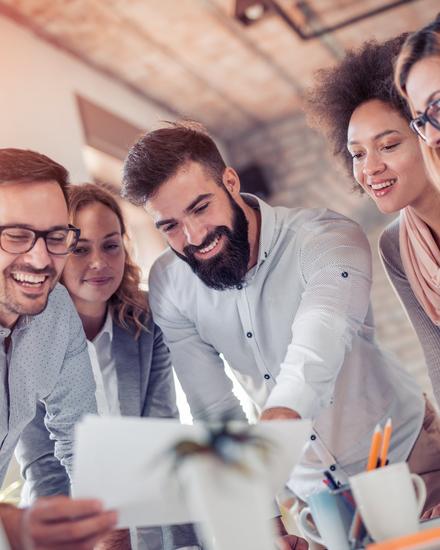 Fünf junge Erwachsene schauen lächelnd auf ein Dokument in einem modernen Büro