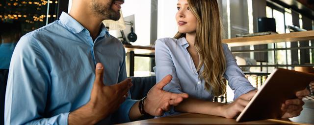 Zwei junge Erwachsene in einem Büro, die sich unterhalten, während die Frau ein Tablet hält