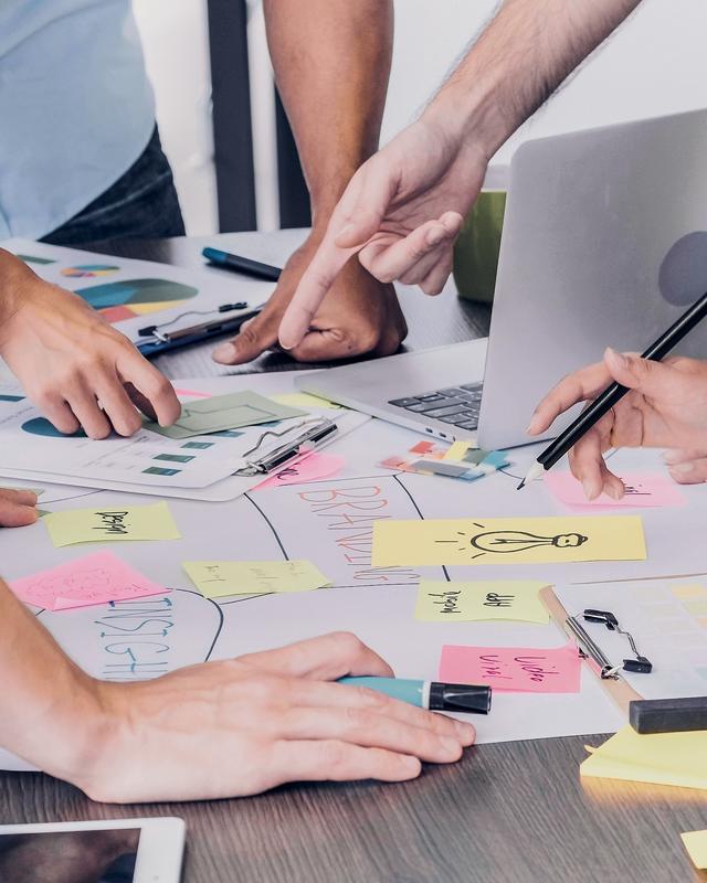 Mehrere Personen arbeiten gemeinsam an einem Tisch mit Notizen, Skizzen und einem Laptop, um Ideen zu entwickeln.