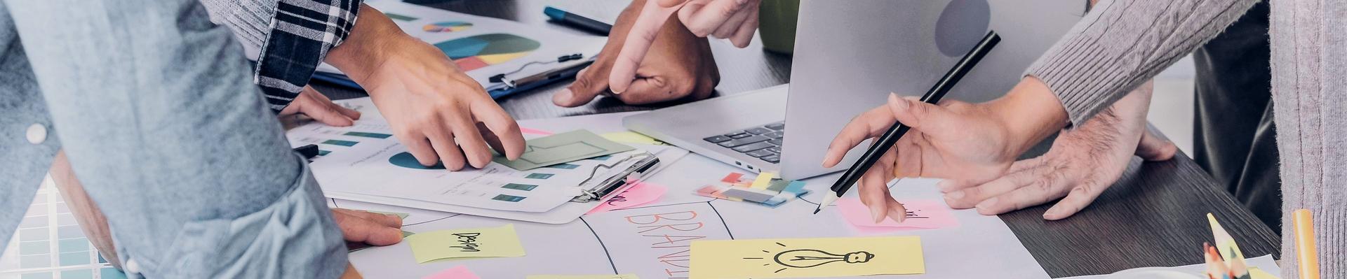 Mehrere Personen arbeiten gemeinsam an einem Tisch mit Notizen, Skizzen und einem Laptop, um Ideen zu entwickeln.