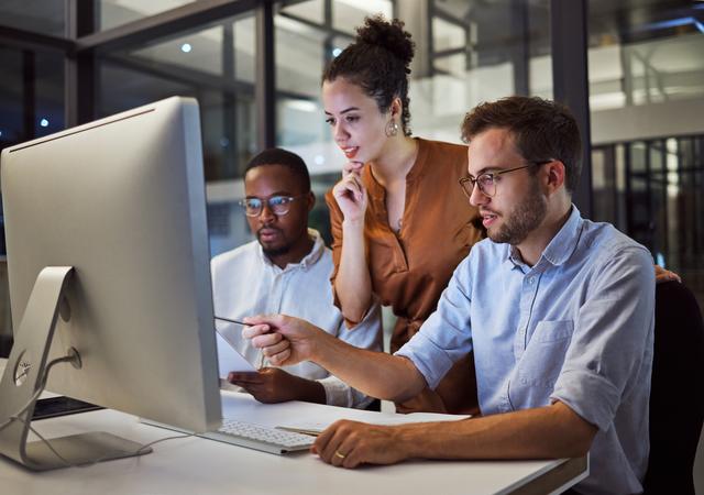 Drei Personen sitzen an einem Schreibtisch und schauen gemeinsam auf einen großen Computerbildschirm Drei Personen sitzen an einem Schreibtisch und schauen gemeinsam auf einen großen Computerbildschirm