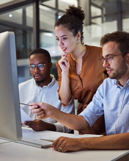 Drei Personen sitzen an einem Schreibtisch und schauen gemeinsam auf einen großen Computerbildschirm