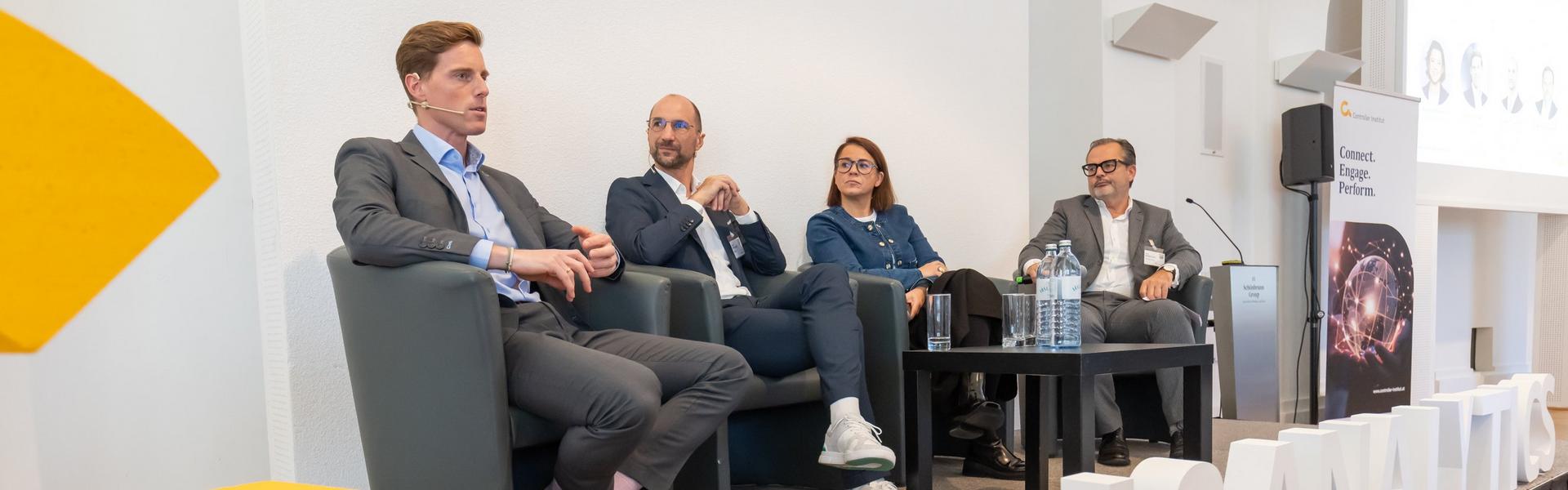 Vier Personen sitzen auf Sesseln auf einer Bühne