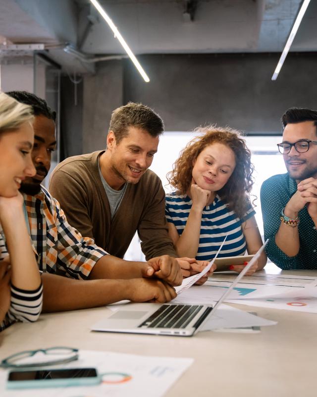 Ein Team von fünf jungen Erwachsenen arbeitete gemensam an einem Tisch mit einem Laptop