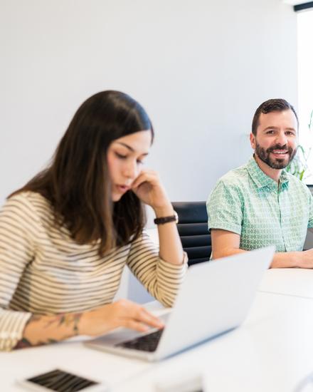 Zwei Personen sitzen an einem Tisch mit Laptops und unterhalten sich