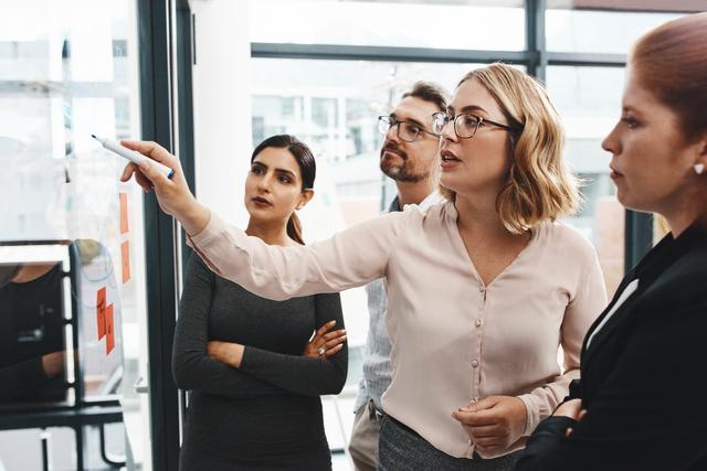 Gruppe von vier Personen in Businesskleidung diskutiert vor einem Whiteboard Gruppe von vier Personen in Businesskleidung diskutiert vor einem Whiteboard