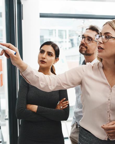 Gruppe von vier Personen in Businesskleidung diskutiert vor einem Whiteboard