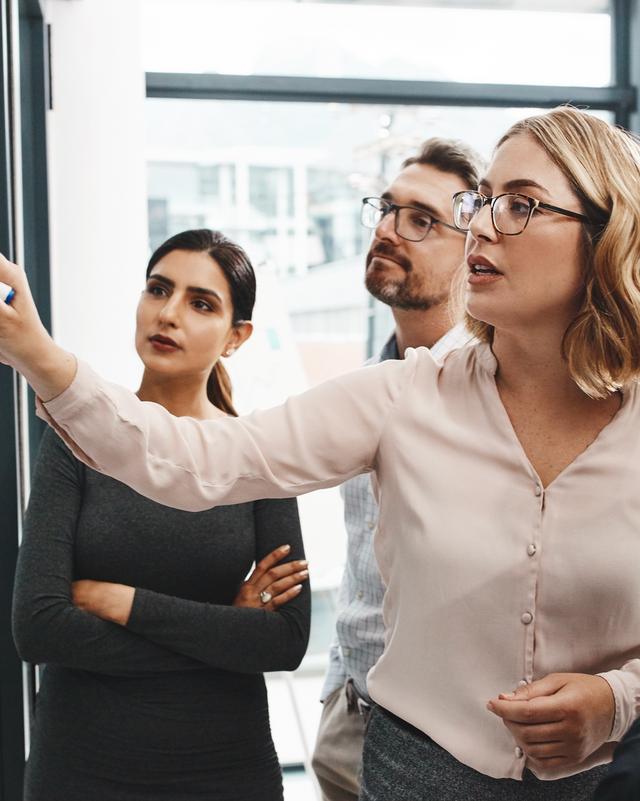 Gruppe von vier Personen in Businesskleidung diskutiert vor einem Whiteboard
