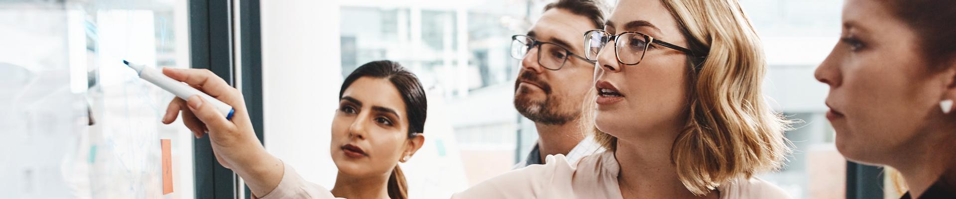 Gruppe von vier Personen in Businesskleidung diskutiert vor einem Whiteboard