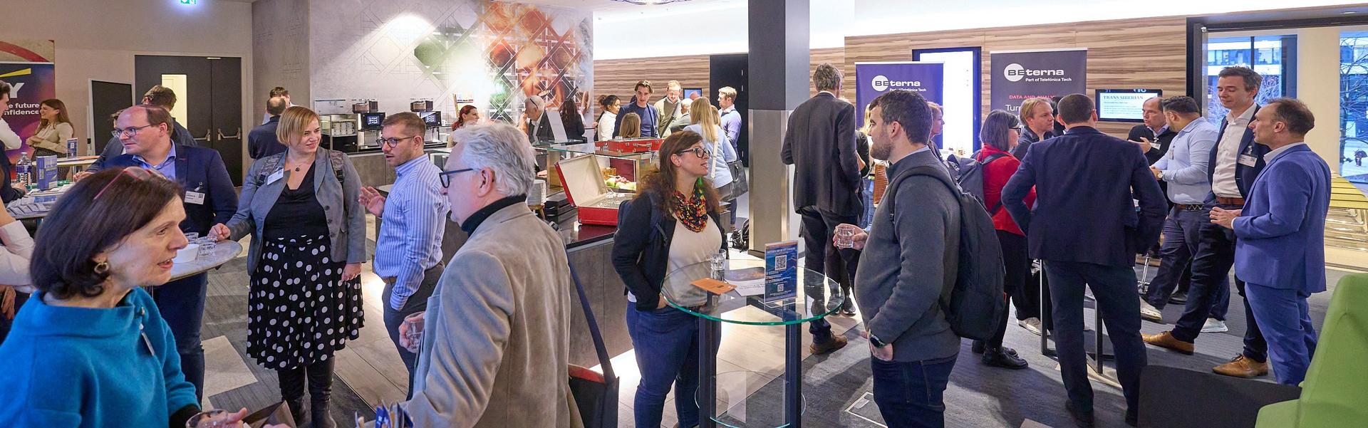 Mehrere Personen unterhalten sich in einem modernen Raum mit Deckenlampen und Informationsständen.