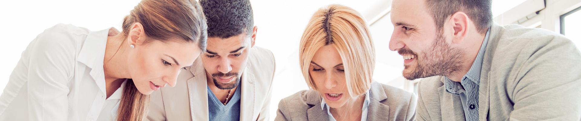 Vier Personen in einem Büro stehen um einen Tisch und betrachten gemeinsam Dokumente