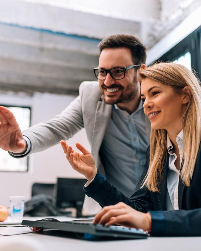 Zwei Personen in einem Büro schauen gemeinsam auf einen Bildschirm und zeigen darauf