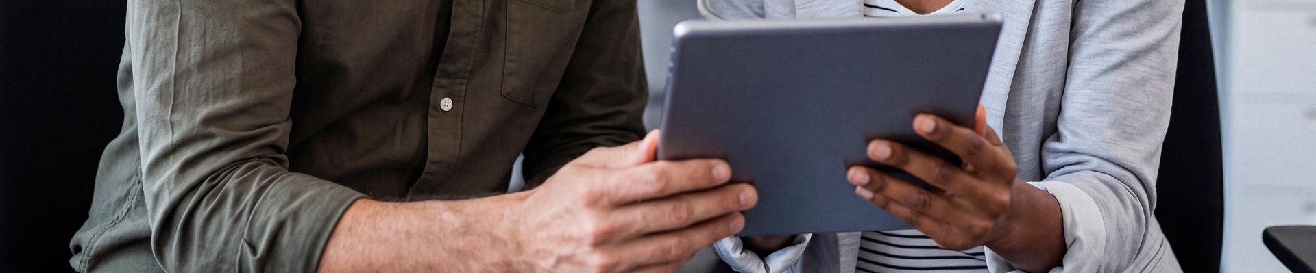 Zwei Personen sitzen nebeneinander und schauen gemeinsam auf ein Tablet Zwei Personen sitzen nebeneinander und schauen gemeinsam auf ein Tablet