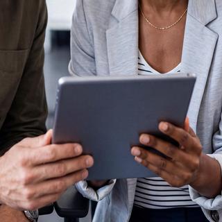 Zwei Personen sitzen nebeneinander und schauen gemeinsam auf ein Tablet
