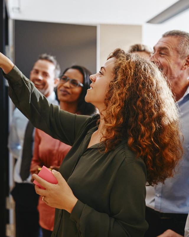 Team von sechs Personen diskutiert und ordnet bunte Haftnotizen an einer Glaswand in einem Büro