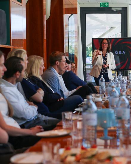 NextGen_MeettheCFO_05_2025 Frau präsentiert vor einer Gruppe von Menschen in einem Meetingraum mit Bildschirm, der 'Q&A' zeigt