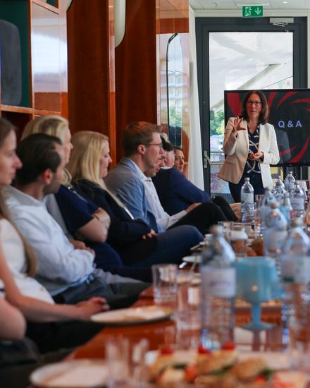 Frau präsentiert vor einer Gruppe von Menschen in einem Meetingraum mit Bildschirm, der 'Q&A' zeigt