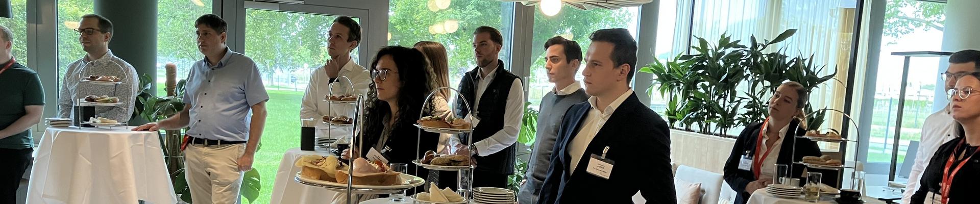 einige Personen, die an festlich geschmückten Stehtischen einem Vortrag zuhören